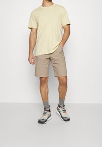 T-shirt à manches courtes jaune clair, short beige et baskets grises avec des accents rouges, portées avec des chaussettes grises. Tenue décontractée au design simple.