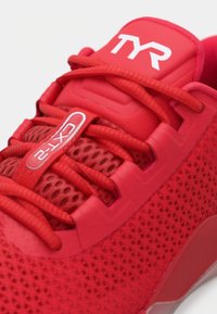 Chaussure de sport rouge avec une tige en mesh respirant, des lacets texturés et une semelle rembourrée avec un logo bien visible sur la languette.