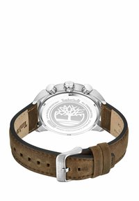 Timberland pulkstenis ar sudraba nerūsējošā tērauda korpusu, brūnu zamša siksnu, trim pogām un gravētu logo aizmugurē. Iespēlē klasisku dizainu.