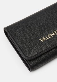 Čierna kožená peňaženka s textúrovaným povrchom, na prednej strane so zlatým logom "VALENTINO". Kompaktná, s preklápacím dizajnom.