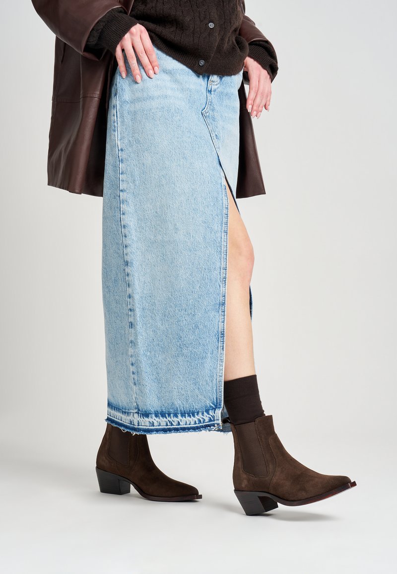 Stivali ankle in suede marrone con punta a punta e tacco a blocco, abbinati a una gonna di jeans azzurro chiaro con spacco laterale e orlo sfrangiato.