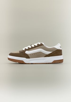 Baskets basses en daim marron clair et marron foncé avec une bande latérale blanche, des lacets blancs et une semelle en caoutchouc couleur gomme sur fond neutre.