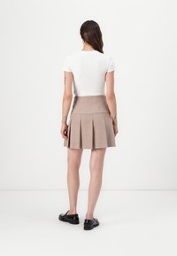 Lightweight beige pleated skirt with a high waistband, made from a textured fabric. Paired with a fitted white short-sleeve top and black shoes.
