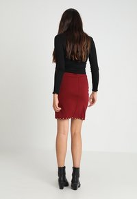 Falda lápiz burdeos con cremallera trasera, con acentos de tachuelas a lo largo del dobladillo. Fabricada con una tela texturizada, diseñada para una silueta ajustada.