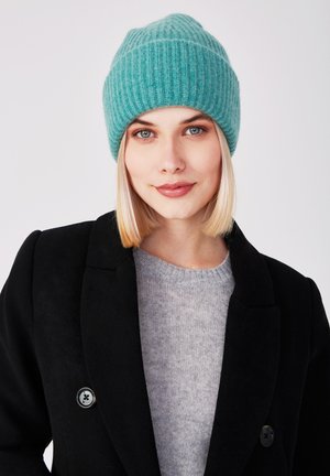 Türkise ribbelte Strickmütze mit einem umgeschlagenen Rand, getragen zu einem schwarzen Mantel und einem grauen Pullover, mit einer glatten Textur und einer engen Passform.