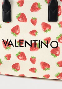 Καμβάς τσάντα tote με σχέδια κόκκινων φραουλών σε κρεμ φόντο, με έντονο μαύρο κείμενο "VALENTINO" και μαύρες δερμάτινες λεπτομέρειες.