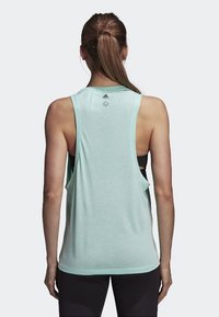Top deportivo de color verde menta claro con un ajuste holgado, diseño de espalda nadadora y detalles recortados. Fabricado con un tejido transpirable ideal para el deporte.