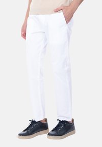 Pantaloni bianchi a gamba affusolata realizzati in cotone, dotati di tasche laterali. Abbinati a sneakers blu scuro con una superficie liscia e dettagli color cuoio.