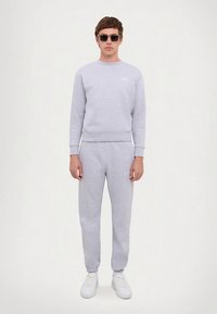 Sudadera de algodón gris y pantalones joggers a juego, ambos con puños acanalados y un diseño sencillo. Zapatillas blancas completan el conjunto.