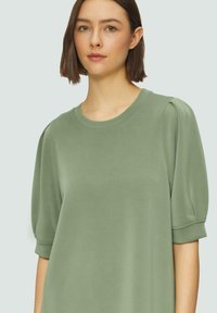 Grünes Kurzarmkleid mit Rundhalsausschnitt, aus glattem Stoff gefertigt. Verfügt über gefütterte Ärmel und eine locker sitzende Passform.