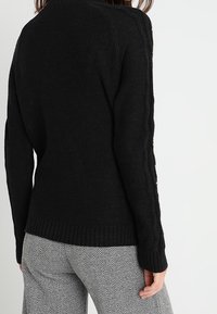 Czarny sweter dziany z prążkowanym dołem i detalami w warkocz wzdłuż rękawów. Nosić over spodni w wzór houndstooth.