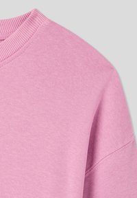 Felpa rosa chiaro con scollatura e polsini a costine. Il materiale sembra morbido; presenta una vestibilità rilassata e una sottile texture.