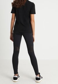 Schwarz T-Shirt und Leggings mit Netzpaneelen. Die Leggings haben eine enge Passform und einen hohen Bund, kombiniert mit schwarz-weißen Sportschuhen.