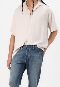 Camicia a maniche corte beige chiaro con una vestibilità rilassata, abbinata a jeans in denim blu con una texture sbiadita e un classico design a cinque tasche.