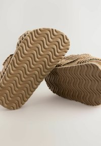 Vävda sandaler med en texturerad brun sula med ett vågigt mönster. Överdelen är tillverkad av naturfiber i en neutral färg.
