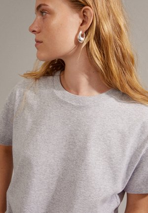 Grey cotton crew-neck t-shirt with short sleeves, featuring a relaxed fit and subtle texture. Accompanied by a shiny silver hoop earring.