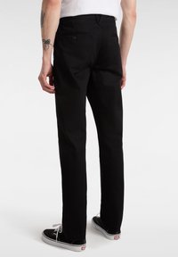 Pantaloni in cotone neri con un design a gamba dritta, dotati di tasche posteriori e vita, abbinati a sneaker nere. Texture liscia.
