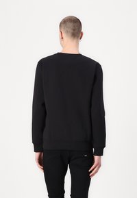 Sudadera negra de manga larga, con puños y dobladillo acanalados, cuello redondo y un diseño minimalista; combinada con jeans negros.