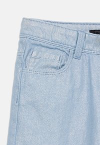Jeans de mezclilla azul claro con un acabado brillante, presillas para el cinturón y un pequeño bolsillo frontal. Se pueden ver detalles de costura limpia a lo largo de los bordes.