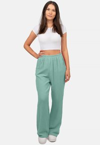 Lichtgroene, gestructureerde wijde broek met een elastische tailleband en zijzakken, gecombineerd met een witte cropped top en witte sneakers.