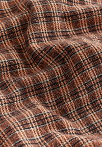 Textil mit einem braun-schwarzen Karomuster, das eine weiche Textur und ein gewebtes Design aufweist und ein schichtartiges Erscheinungsbild erzeugt.