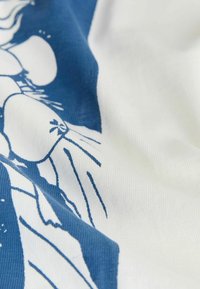 Nahaufnahme eines weißen Stoffs mit blauem Blumenmuster, das große Blütenblätter und dünne Stängel zeigt, mit sichtbarer Stoffstruktur und sanften Falten.