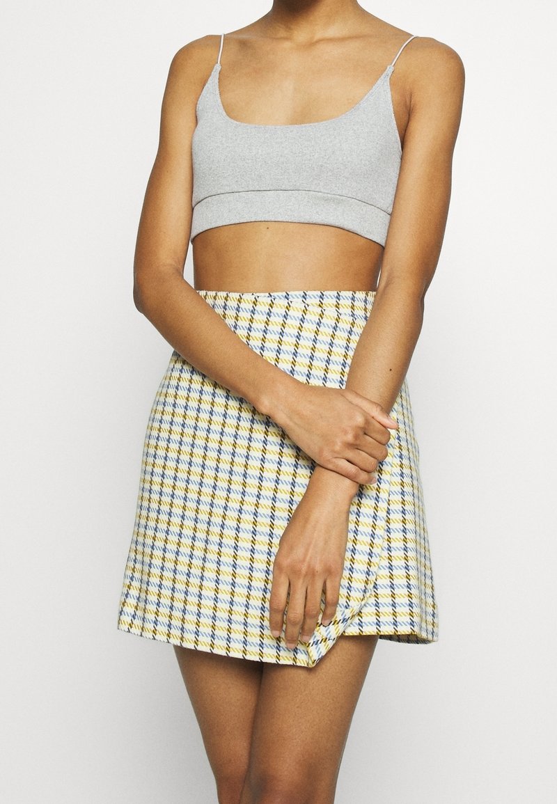 Top court gris associé à une mini-jupe à carreaux jaune, bleue et blanche. La jupe présente un ourlet qui s'incurve légèrement vers le haut.