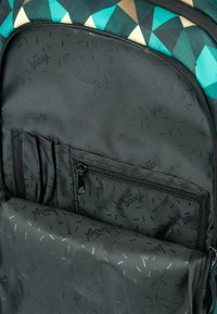 Černý textilní interiér batohu s kapsou na zip a různými přihrádkami. Obsahuje vzorovanou podšívku s nenápadně vytištěným názvem značky.