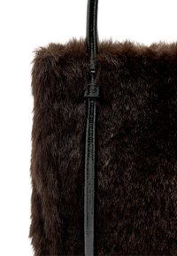 Brązowa torba typu tote z futerkiem z imitacji futra i błyszczącą czarną rączką. Tekstura jest miękka i puszysta, pasek ma gładkie wykończenie.