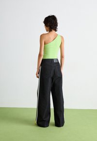 Groene, één-schouder fitted top gecombineerd met hooggetailleerde, wijde zwarte jeans met zijstrepen en een zichtbaar merklabel op de achterkant.