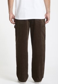 Brune corduroy cargo bukser med en afslappet pasform, som har sidelommer og en blød, tekstureret overflade. Bæres med en hvid t-shirt og sneakers.
