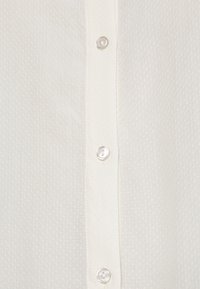 Camicia bianca con bottoni, caratterizzata da un tessuto testurizzato con un motivo sottile, soffietti verticali e bottoni rotondi e lucidi.