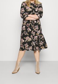 Black floral dress with three-quarter sleeves, featuring a collar and a flowy silhouette. Worn with beige ankle boots.