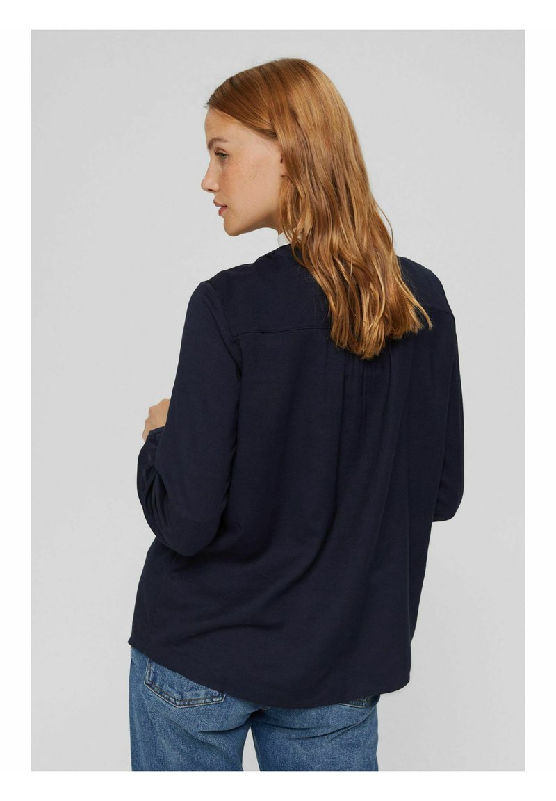 Marineblaue Langarmshirt mit runder Ausschnitt, Rückenplissee und lockerer Passform. Aus weichem Stoff gefertigt, kombiniert mit blauen Jeans.