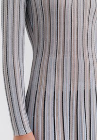 Dzianinowa sukienka z długim rękawem w pionowe paski w kolorach jasnoniebieskim, czarnym i beżowym. Faktura tkaniny tworzy prążkowany wygląd wzdłuż tułowia.