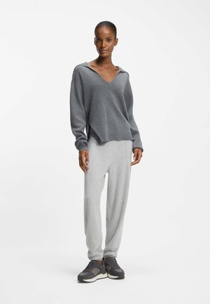 Gray hooded sweater with V-neck, asymmetrical hem. Paired with light gray joggers and dark gray sneakers. Smooth texture and relaxed fit.