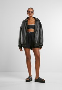 Černá kožená bomber bunda, černý zkrácený top a černé volné šortky. Modelka má na sobě tmavě zabarvené sluneční brýle a černé platformové sandály.