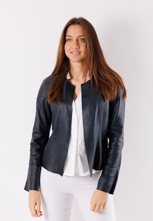 Giacca in pelle blu navy con una texture liscia, design con apertura frontale e maniche lunghe, abbinata a una camicia bianca e pantaloni chiari.