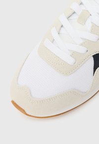 Sneaker z białą siateczkową cholewką z beżowymi zamszowymi akcentami i ciemnoniebieskimi detalami. Białe sznurówki i podeszwa z gumy kończą ten projekt.