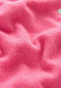 Lyserødt strikket stof med en glat tekstur, der viser fine tråde og lette farvevariationer, samlet i bløde folder.