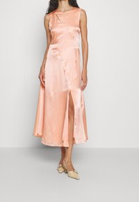 Satin, ärmlös, ankellång klänning i mjuk persika, med en sidoklyvning och en asymmetrisk detalj med utfällning fram.