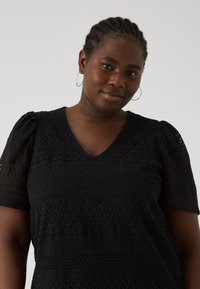 Black, textured blouse featuring a V-neck, short puff sleeves, and intricate lace-like patterns throughout the fabric.