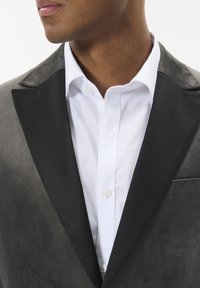 Mand iført en sort fløjl smokingjakke med satinklapper over en hvid skjorte, vist fra halsen til midt på torsoen.