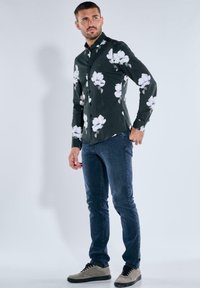 Schwarzes Blumen-Hemd mit weißen Blumen, kombiniert mit dunkelblauen Jeans und grauen Sneakers. Verfügt über lange Ärmel und ein tailliertes Design.