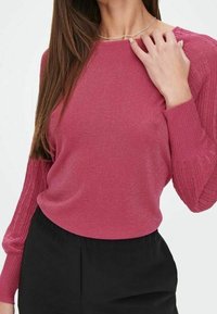 Haut à manches longues côtelé magenta avec un éclat texturé, encolure ronde et silhouette ajustée, associé à un pantalon noir.