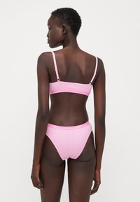 Pink ribbed bralette with adjustable straps and matching high-waisted bikini bottom, featuring a smooth, stretchy texture and minimal design.