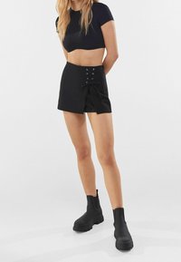 Pantalones cortos negros con una abertura lateral y detalle de cordones, combinados con botines negros. La tela tiene una textura suave y un diseño ajustado.