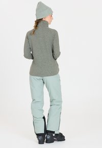 Lys grøn pullover med høj krave, parret med lyseblå snebukser og sorte skistøvler. Har ribbet beanie og struktureret stof.