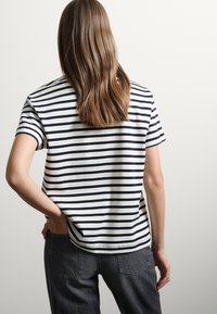 Gestreepte T-shirt met korte mouwen in zwart en wit, met een ronde zoom en een losvallende pasvorm, gecombineerd met hoogdrachtige donkergrijze jeans.