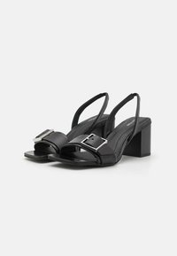 Black slingback heels made of smooth leather with a square silver buckle, featuring a block heel and open-toe design.